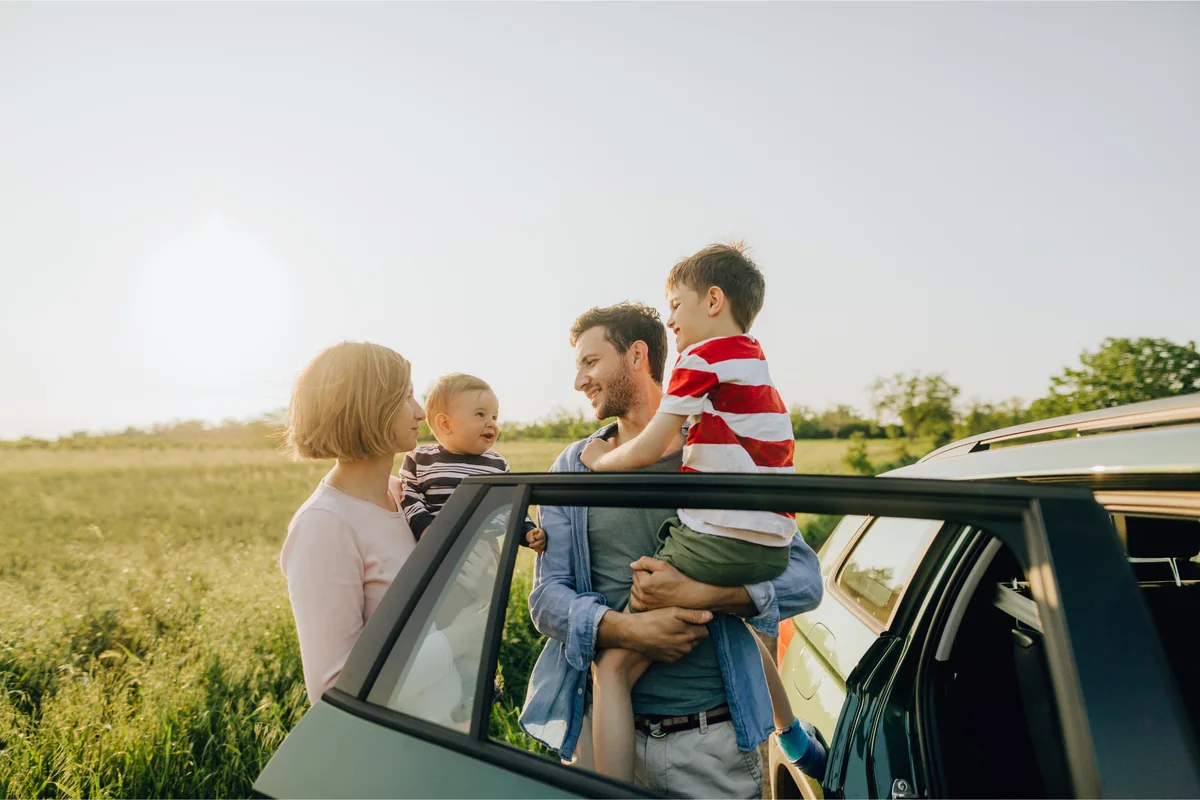 A family standing beside their car in a sunlit field, smiling together